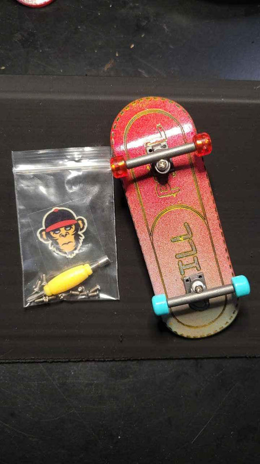Red custom fingerboard with blue wheels, a monkey sticker, and a tool in a plastic bag.