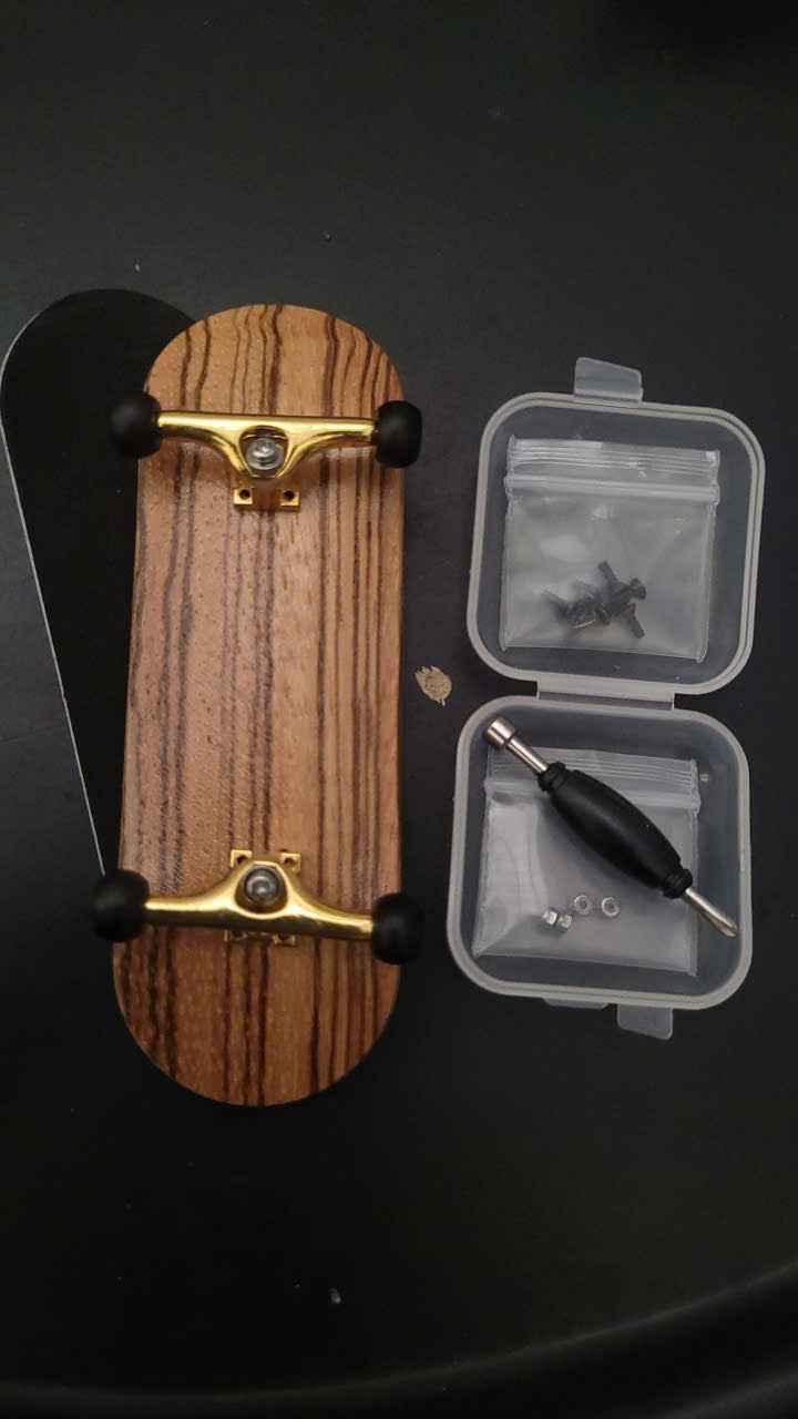 Custom wooden fingerboard deck with gold trucks, black wheels, and assembly tools.