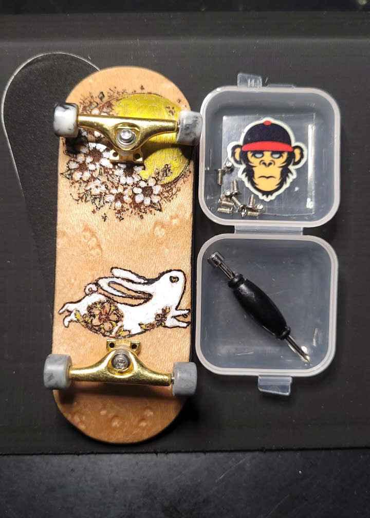 Custom handmade fingerboard deck with rabbit graphic, gold trucks, and mini tool kit.