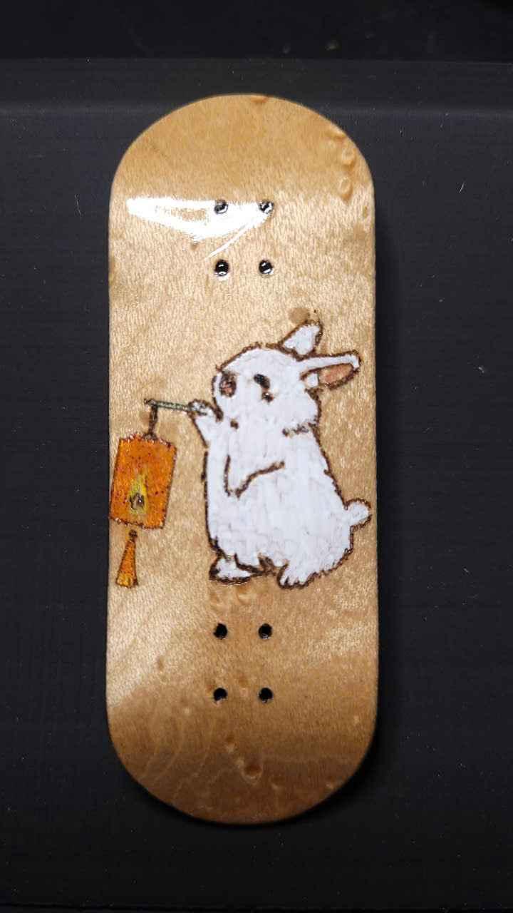 Handmade wooden fingerboard deck featuring a white bunny holding an orange lantern.