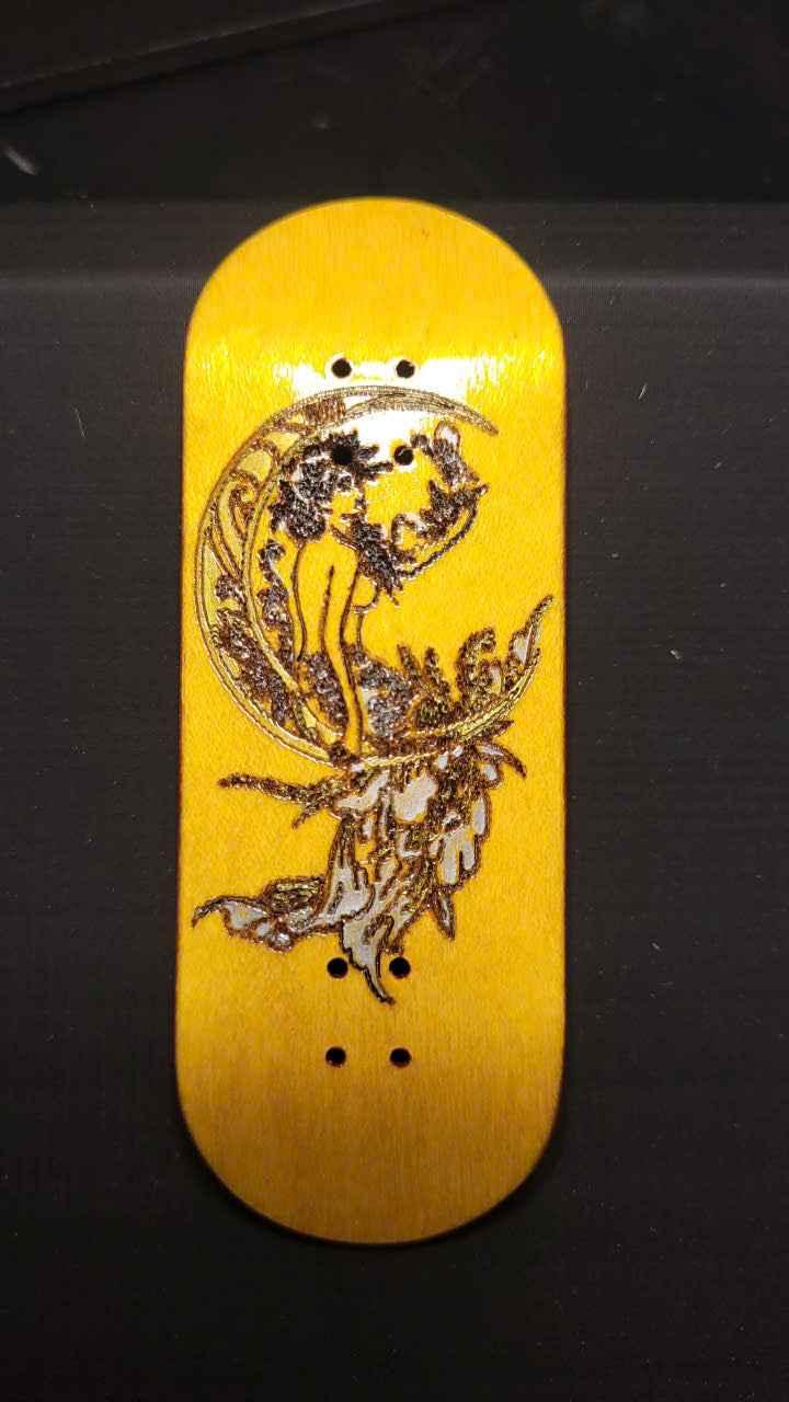 Custom handmade fingerboard deck with celestial moon and figure graphic on yellow wood.