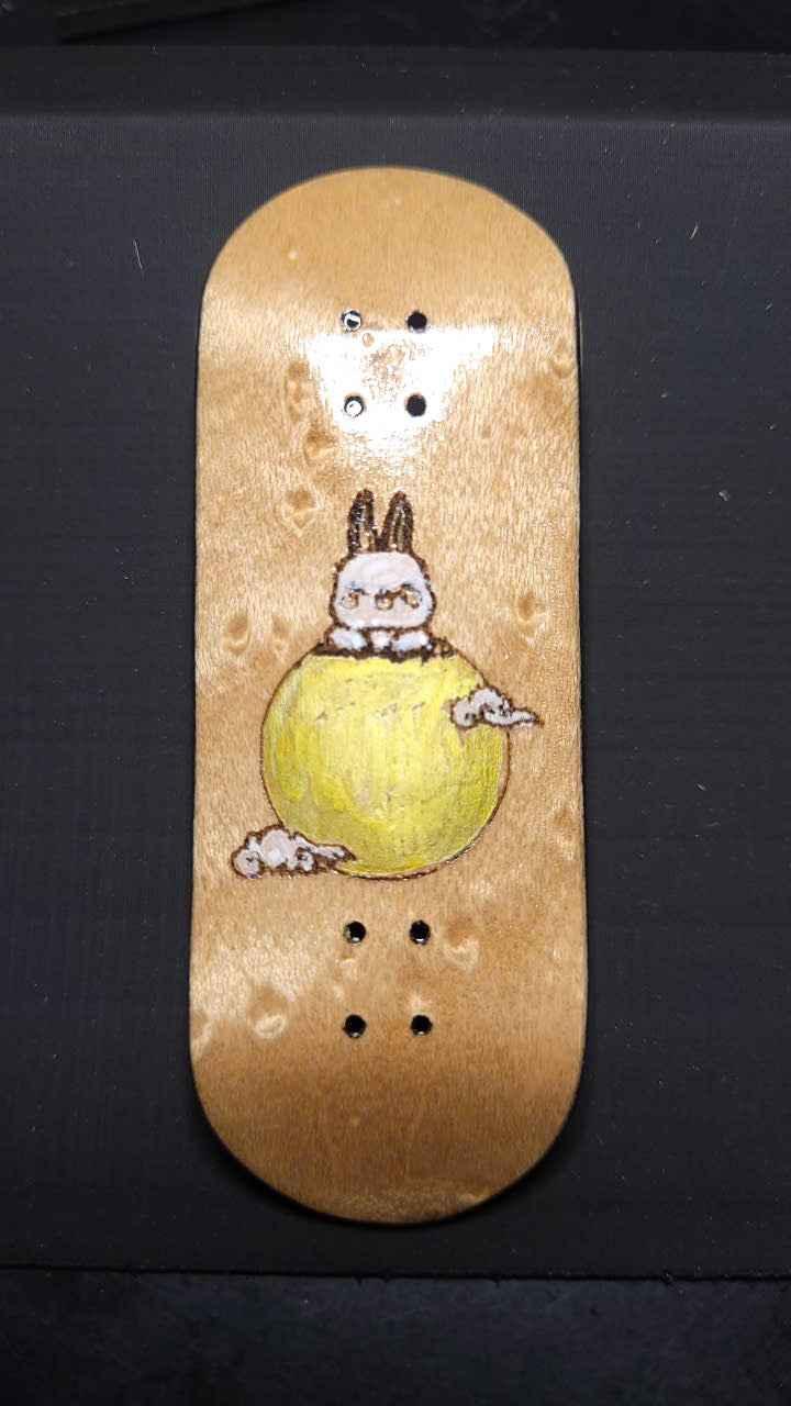 Handmade wooden fingerboard deck featuring a custom bunny illustration on a yellow ball.