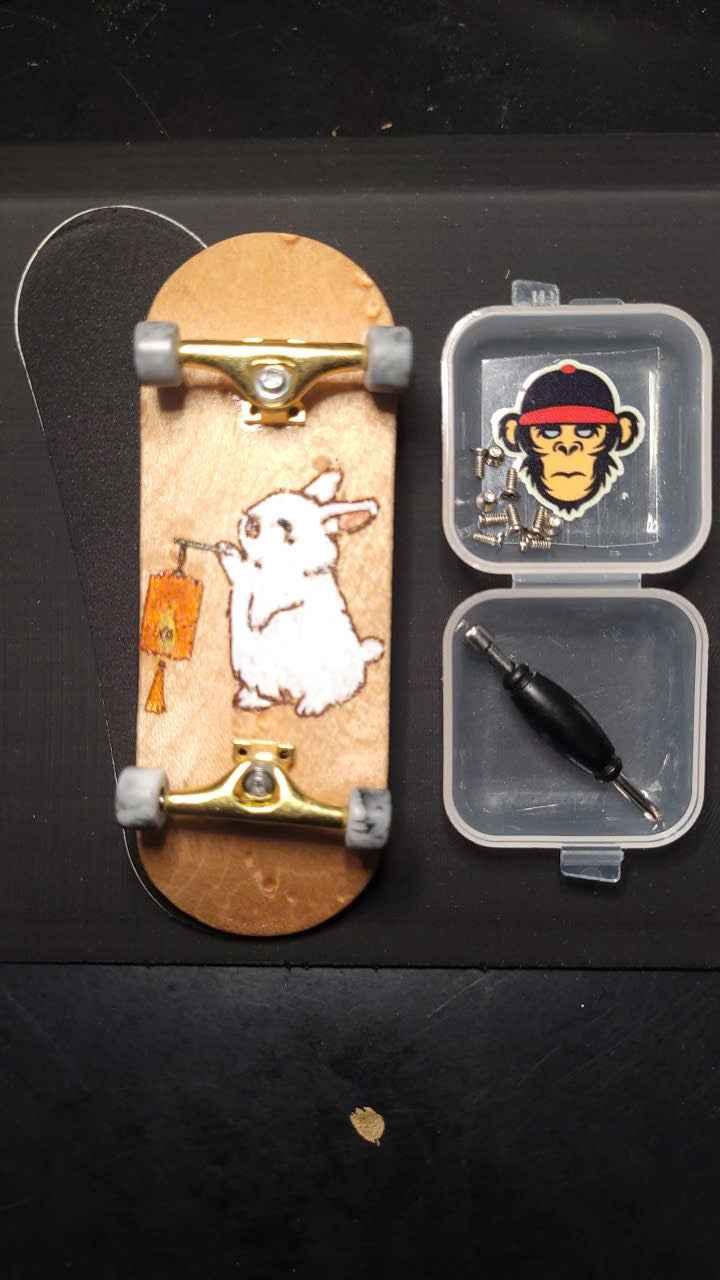 Custom handmade fingerboard deck with rabbit graphic, gold trucks, and mini tool kit.