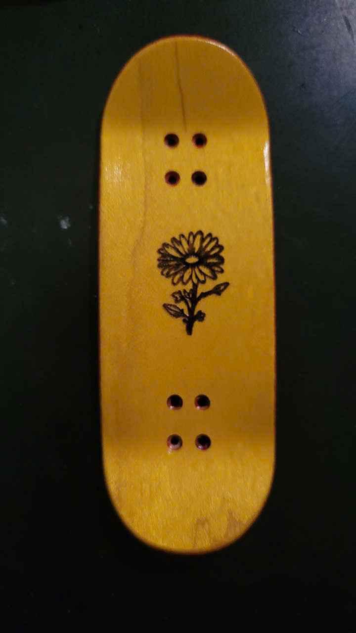 Handmade wooden fingerboard deck with a black flower graphic on a natural wood finish.