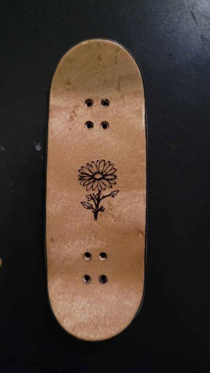 Custom handmade wooden fingerboard deck with a black daisy flower graphic.
