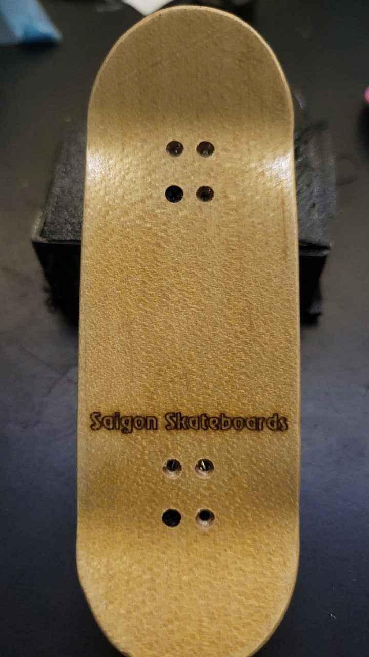 Handmade wooden fingerboard deck with Saigon Skateboards logo on a dark surface.