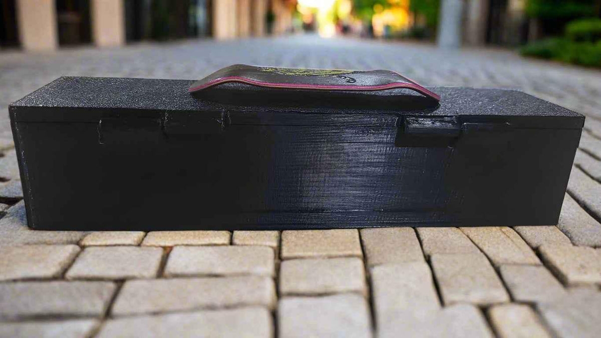 Custom handmade fingerboard deck resting on a black storage box outdoors.