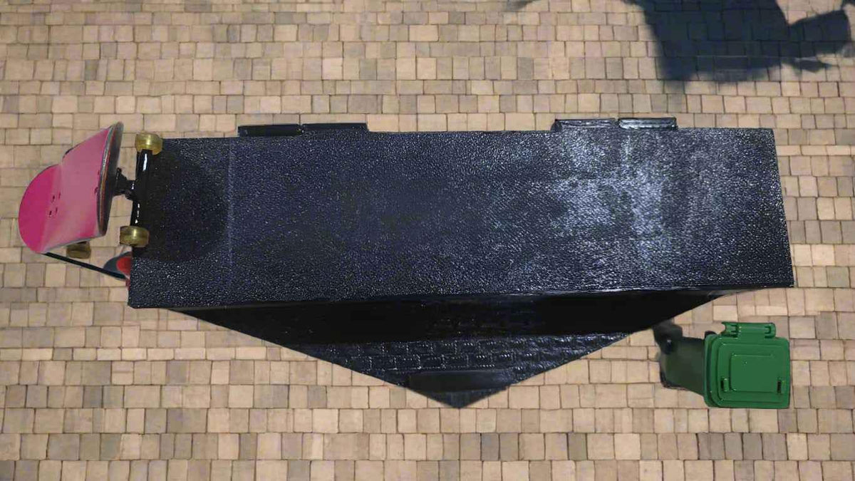 A pink fingerboard performing a trick on a black miniature skate ramp.