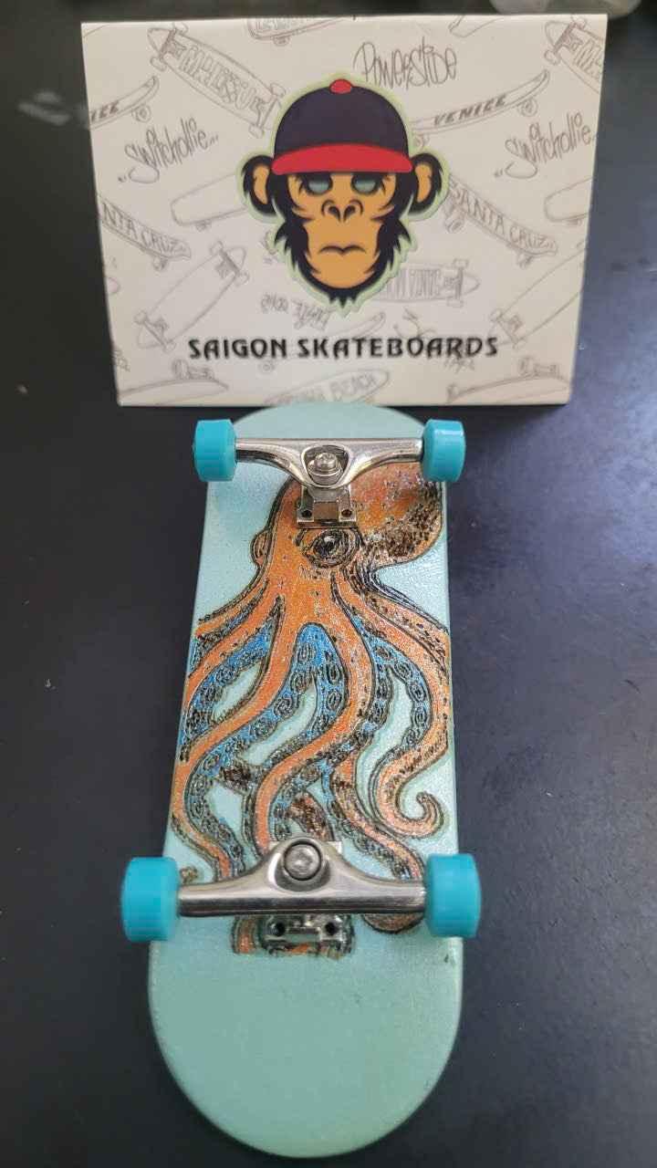 Custom handmade fingerboard deck with octopus graphic and light blue wheels.