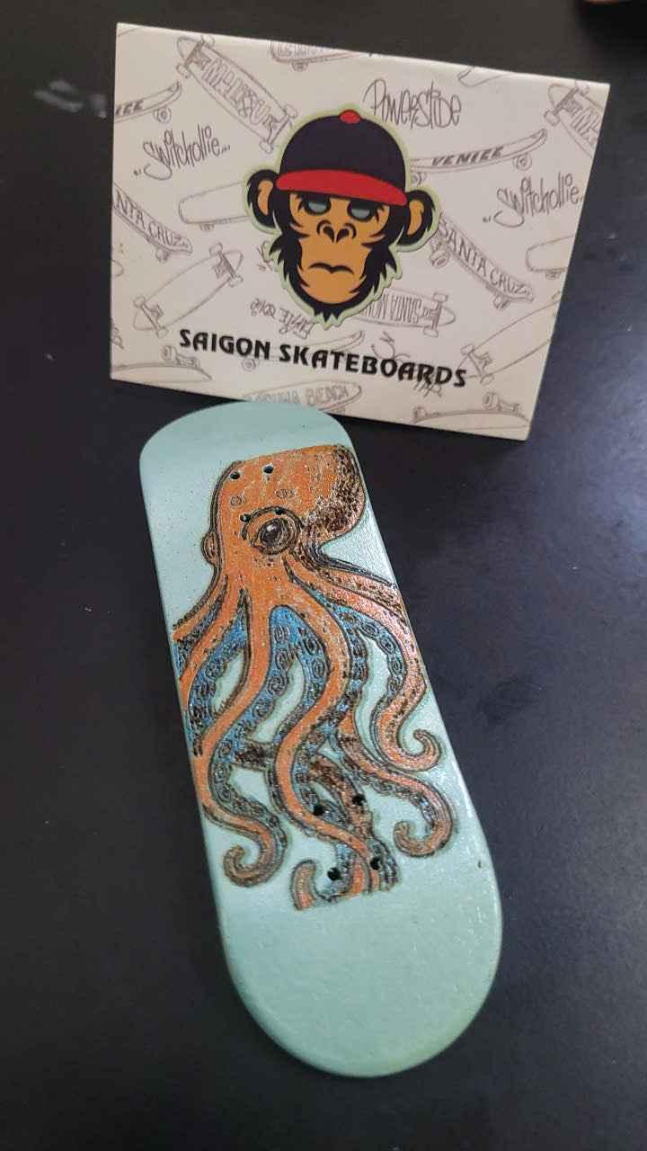 Handmade custom fingerboard deck with orange octopus graphic on light blue wood.