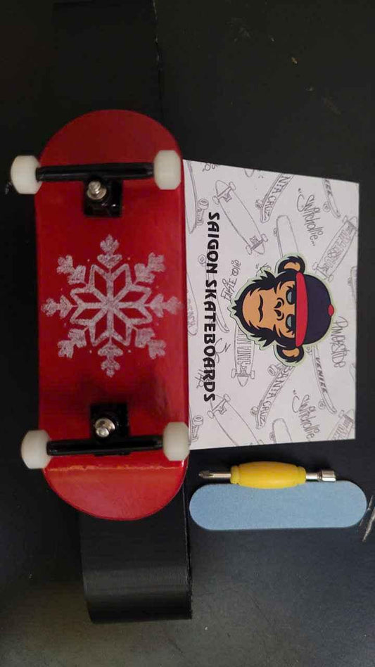 Red custom fingerboard deck with snowflake graphic, trucks, wheels, and skate tool.