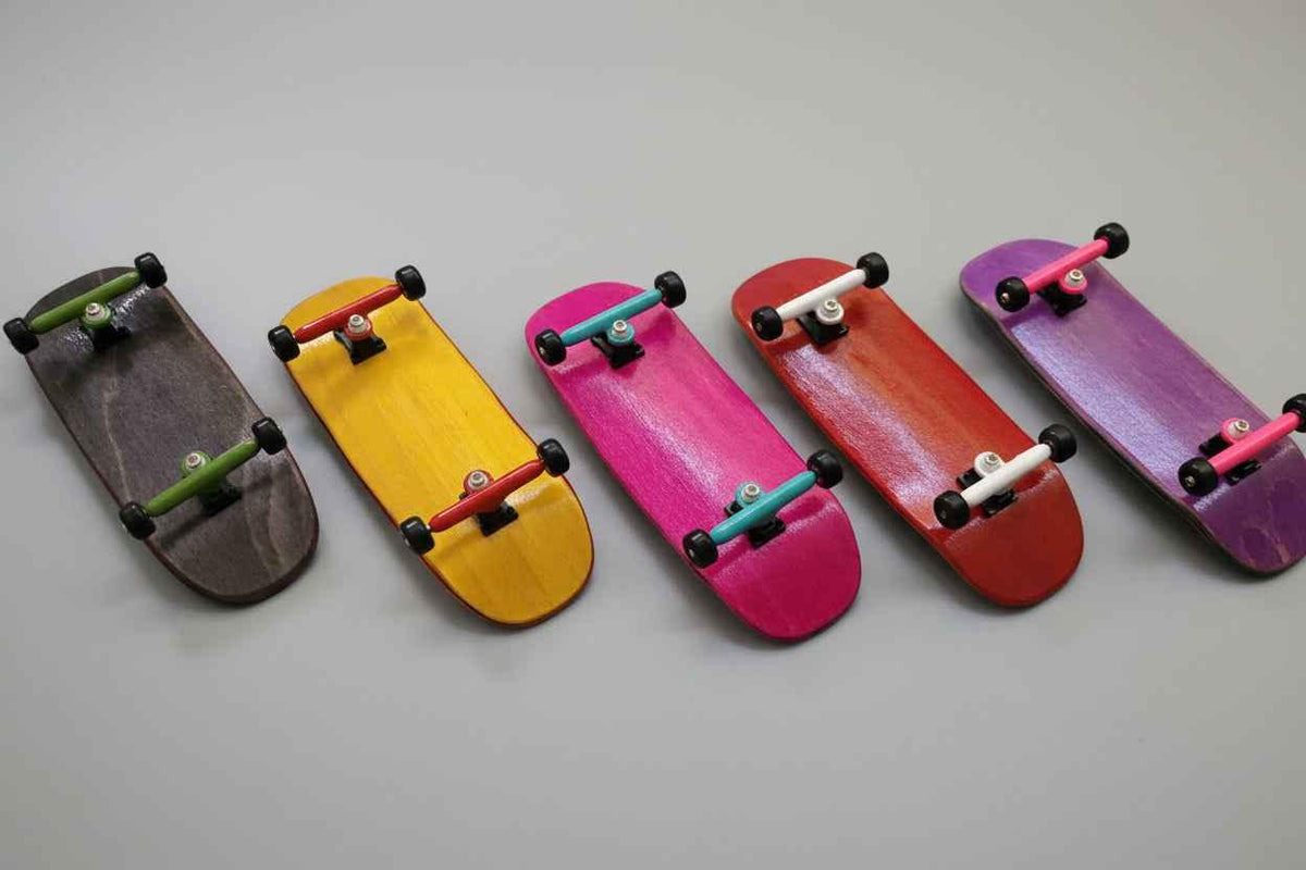 Five colorful handmade custom fingerboard decks lined up on a grey surface.