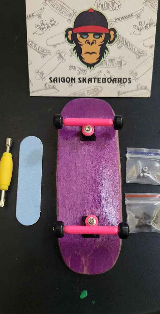 Custom purple fingerboard deck with pink trucks, tools, and accessories on a black surface.