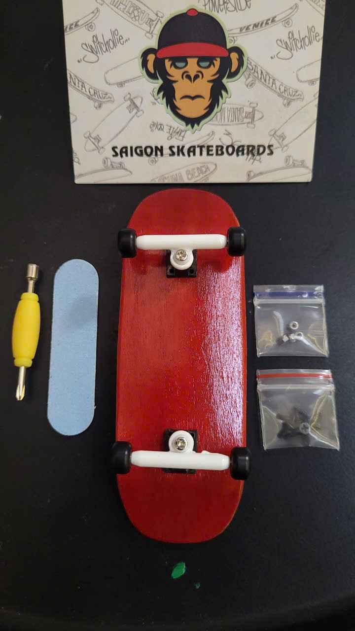 Red custom fingerboard deck with trucks, wheels, grip tape, and tool on a black background