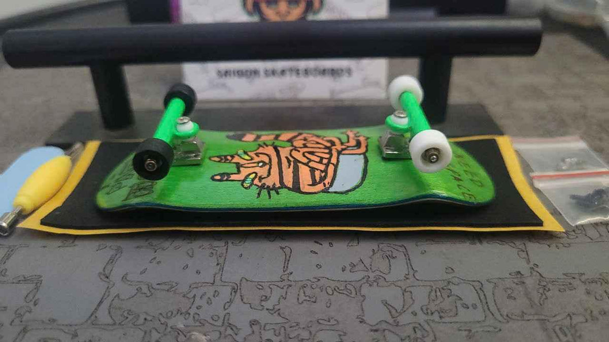 Custom handmade green fingerboard deck with graphic art and white wheels on a rail.