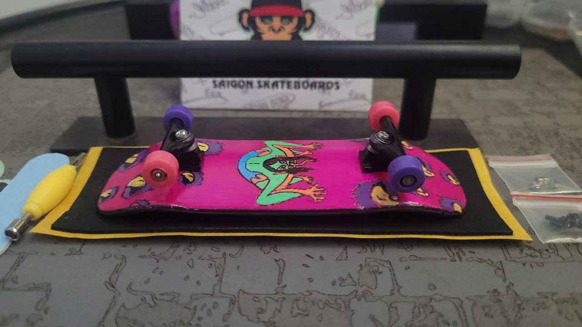 Custom pink graphic fingerboard deck with colorful wheels on a black mat.