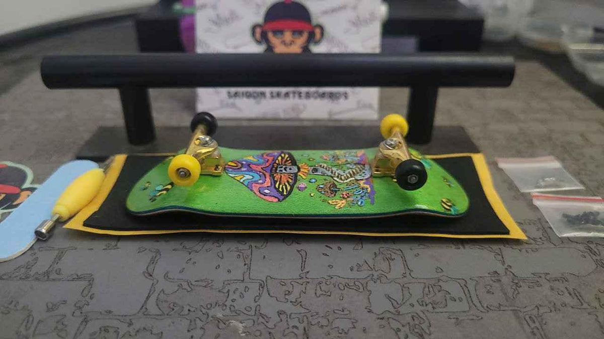 Custom handmade green fingerboard deck with colorful graphic and yellow wheels.