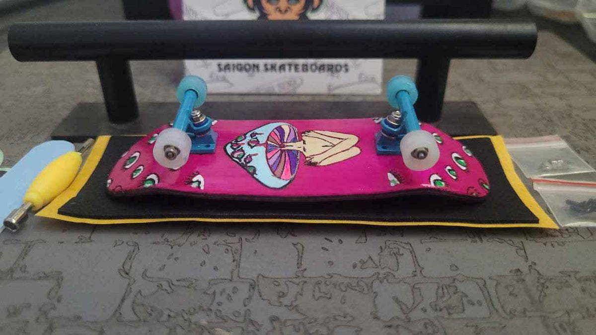 A custom pink fingerboard with graphic art on a black mat near a fingerboard rail.