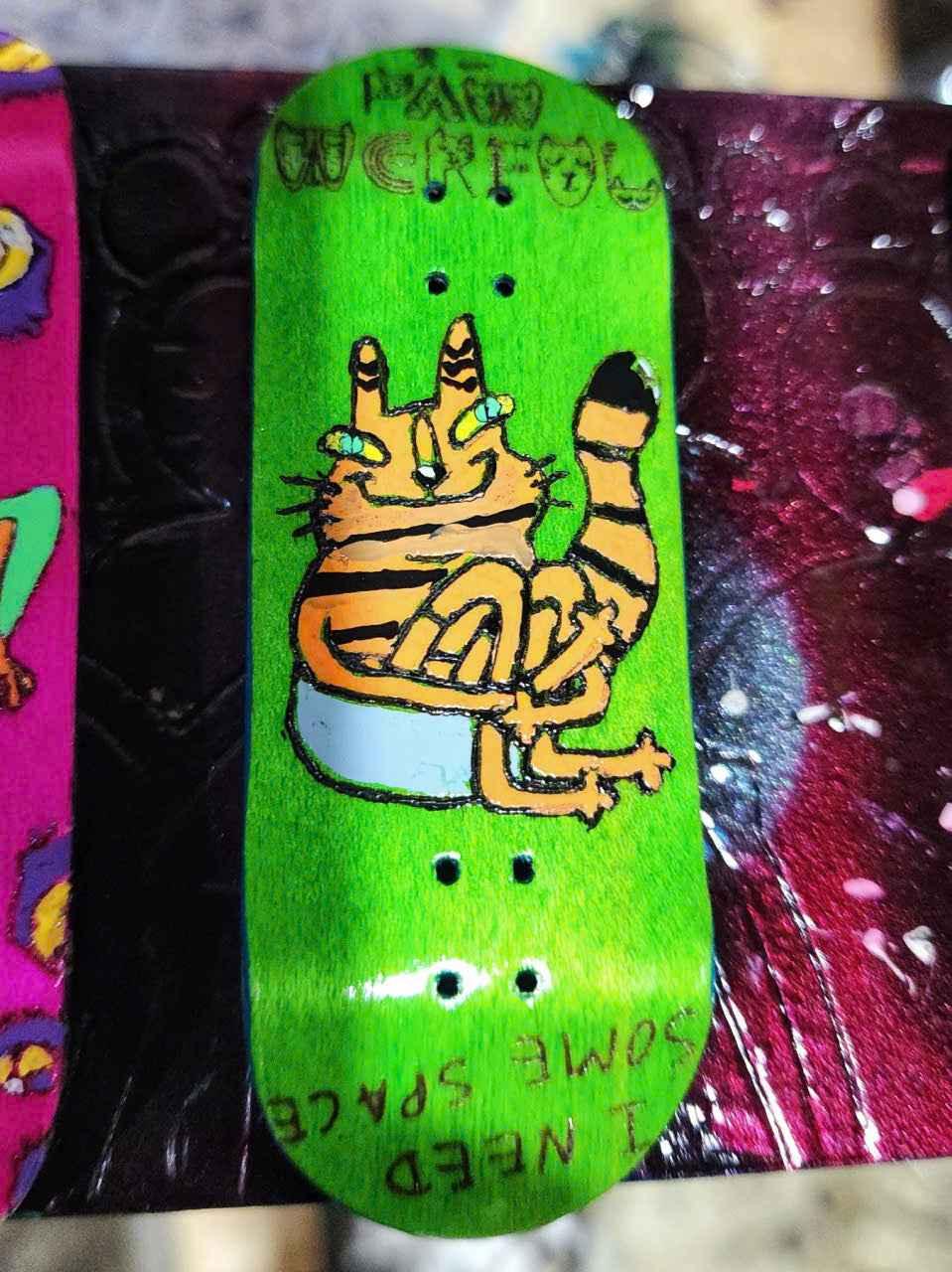 Green custom fingerboard deck featuring a cartoon orange cat illustration.