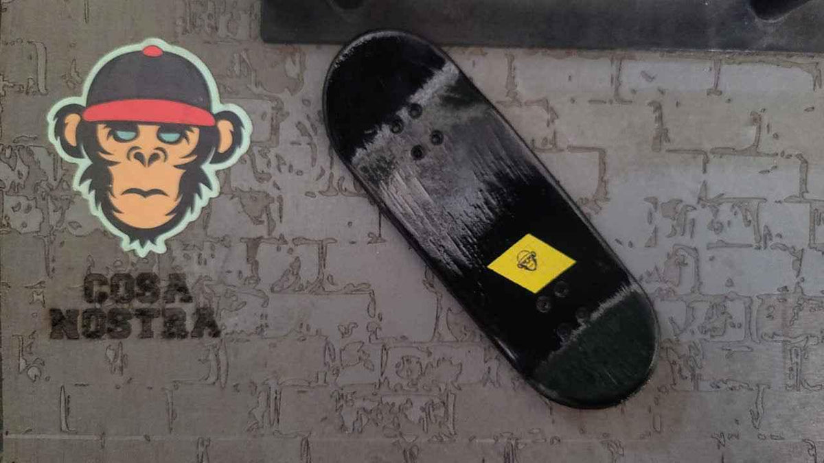 Black custom fingerboard deck with a small yellow diamond logo on a textured surface.