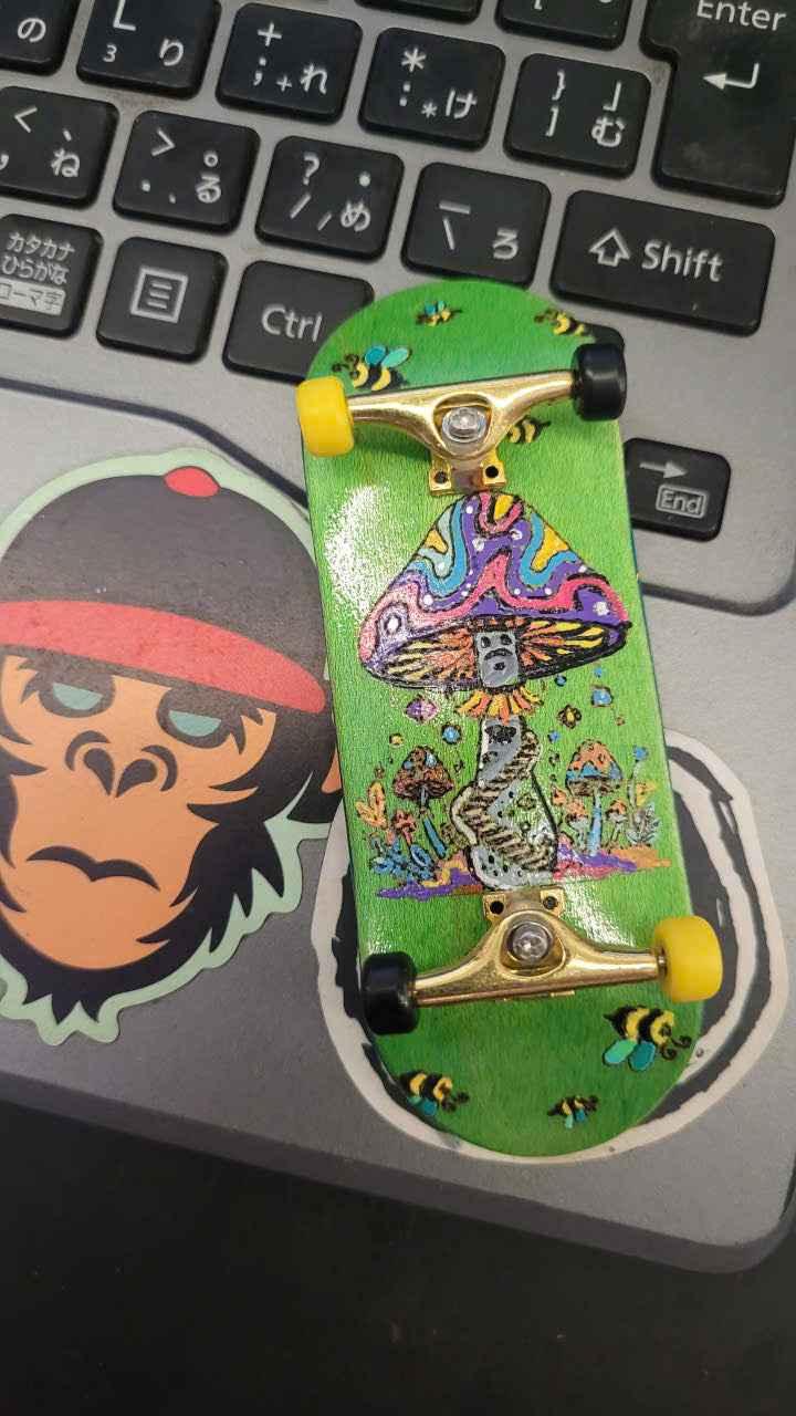 Custom handmade fingerboard deck with colorful psychedelic mushroom graphic on a laptop.