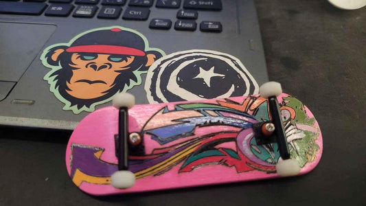 Custom pink handmade fingerboard deck with colorful graphic design on a laptop.
