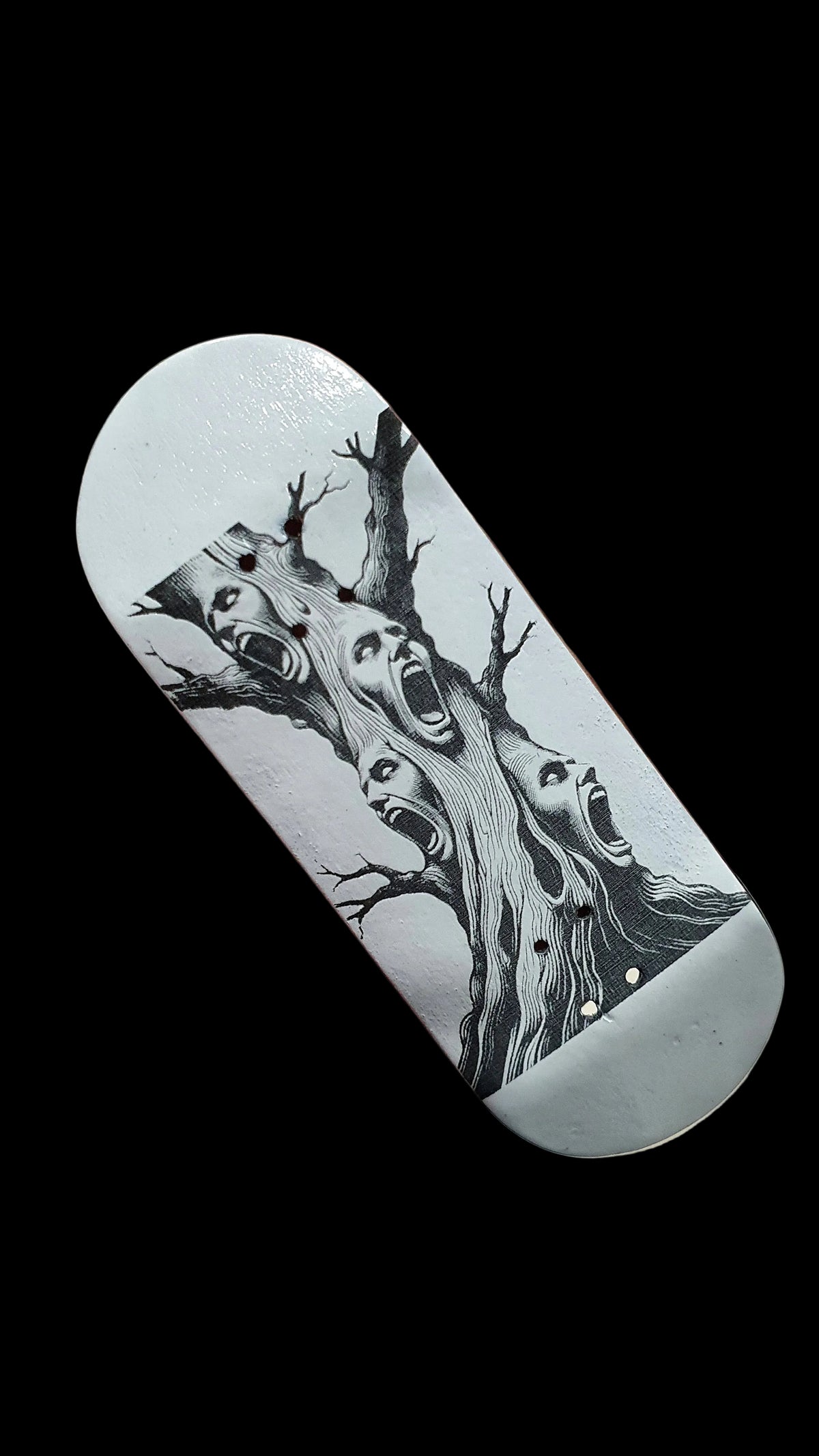 Light gray skateboard deck angled, black-and-white tree and screaming faces graphic