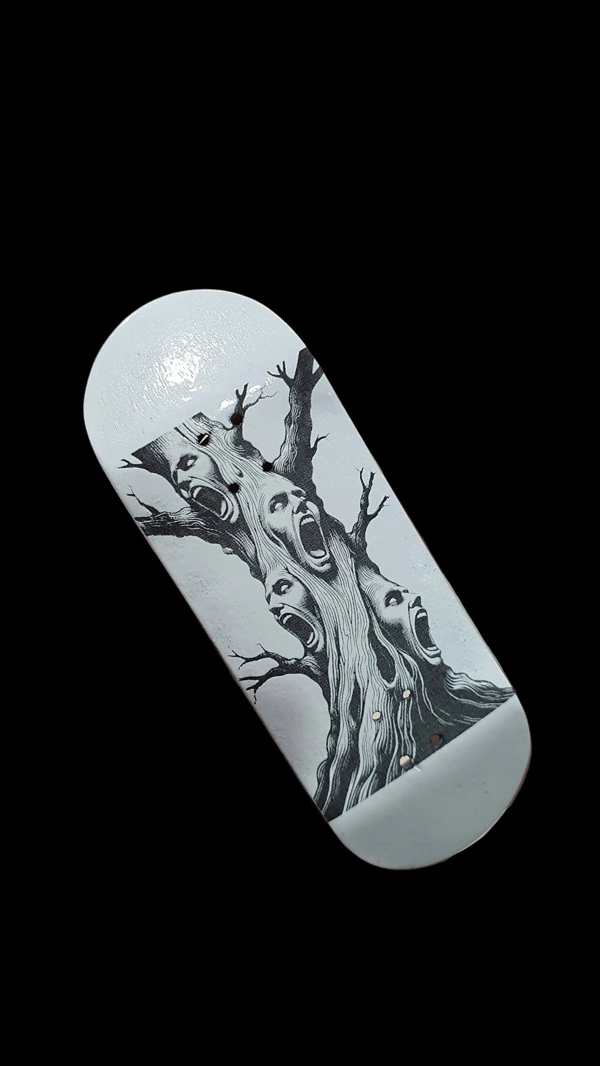 Skateboard deck angled view with black tree-face graphic on pale surface