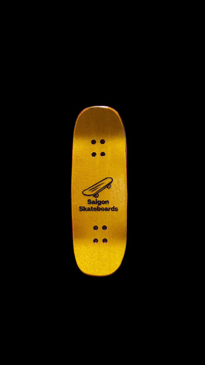 Yellow maple underside of a Saigon Skateboards fingerboard deck with logo and mounting holes