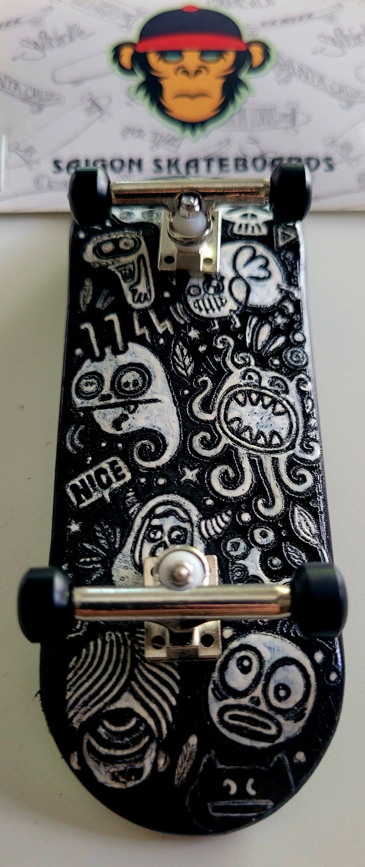 Black medium fingerboard with white monster doodle graphics and silver trucks.