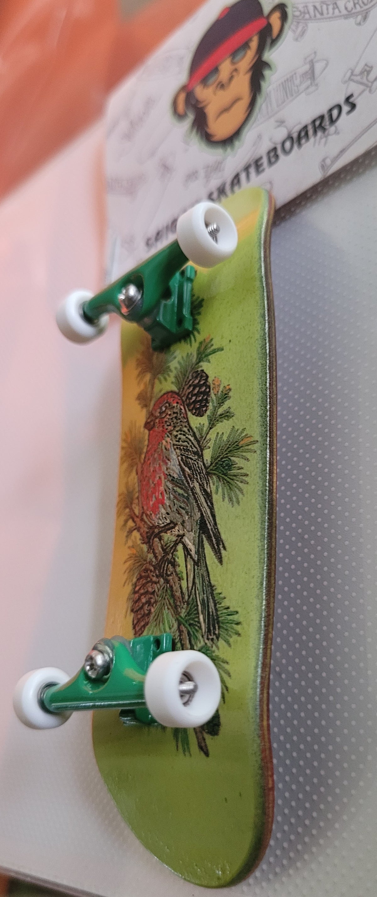 Green fingerboard with bird artwork and white wheels on green trucks