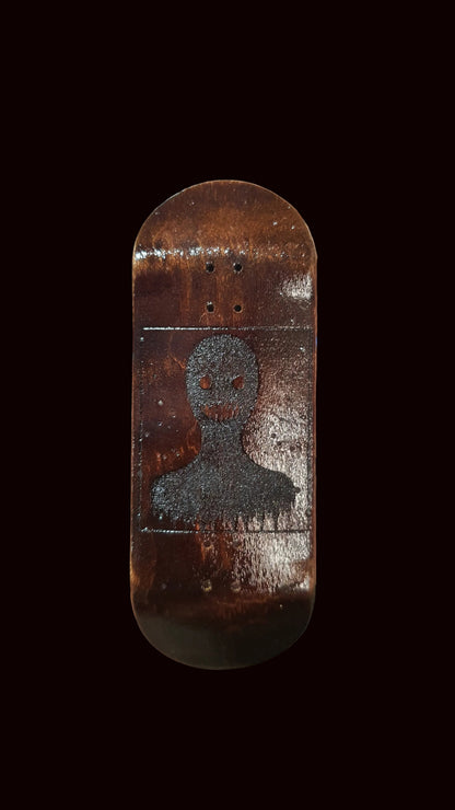 Hand holding a small wooden skateboard deck with a design on a blurred background
