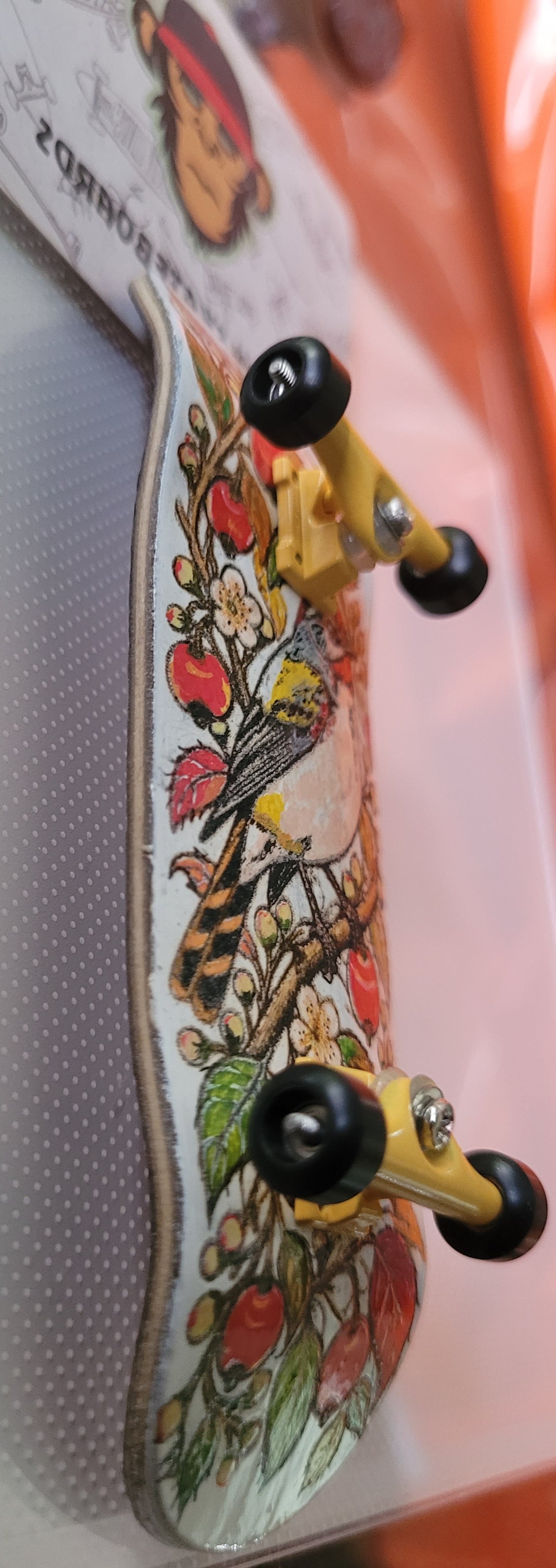 Side view of complete finger skateboard with bird graphic deck and trucks