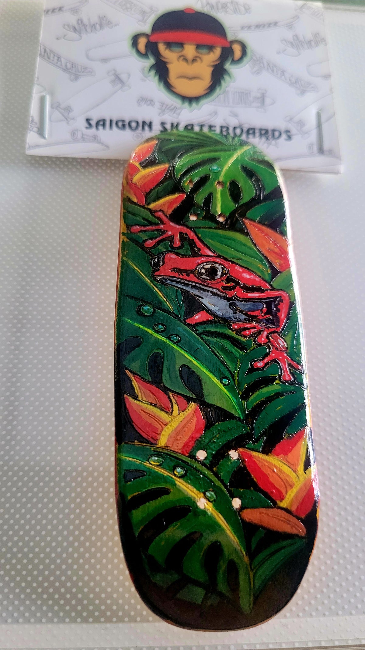 Green jungle fingerboard deck with red lizard illustration and orange leaf accents