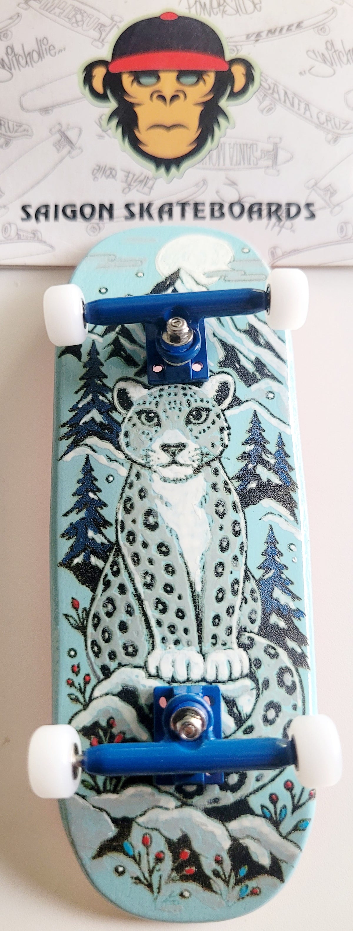 Teal finger skateboard with snow leopard artwork, blue trucks, white wheels