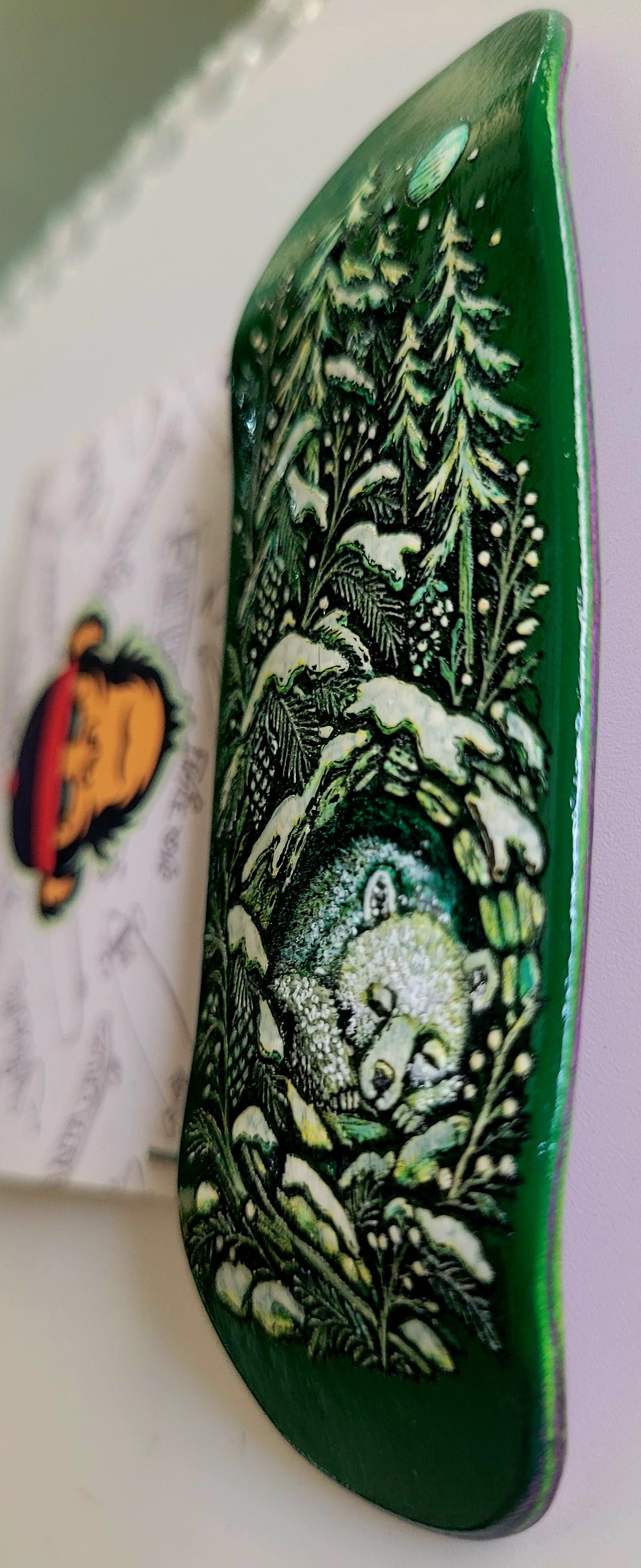 Dark green skateboard deck side view with detailed forest, moon, and animal illustration