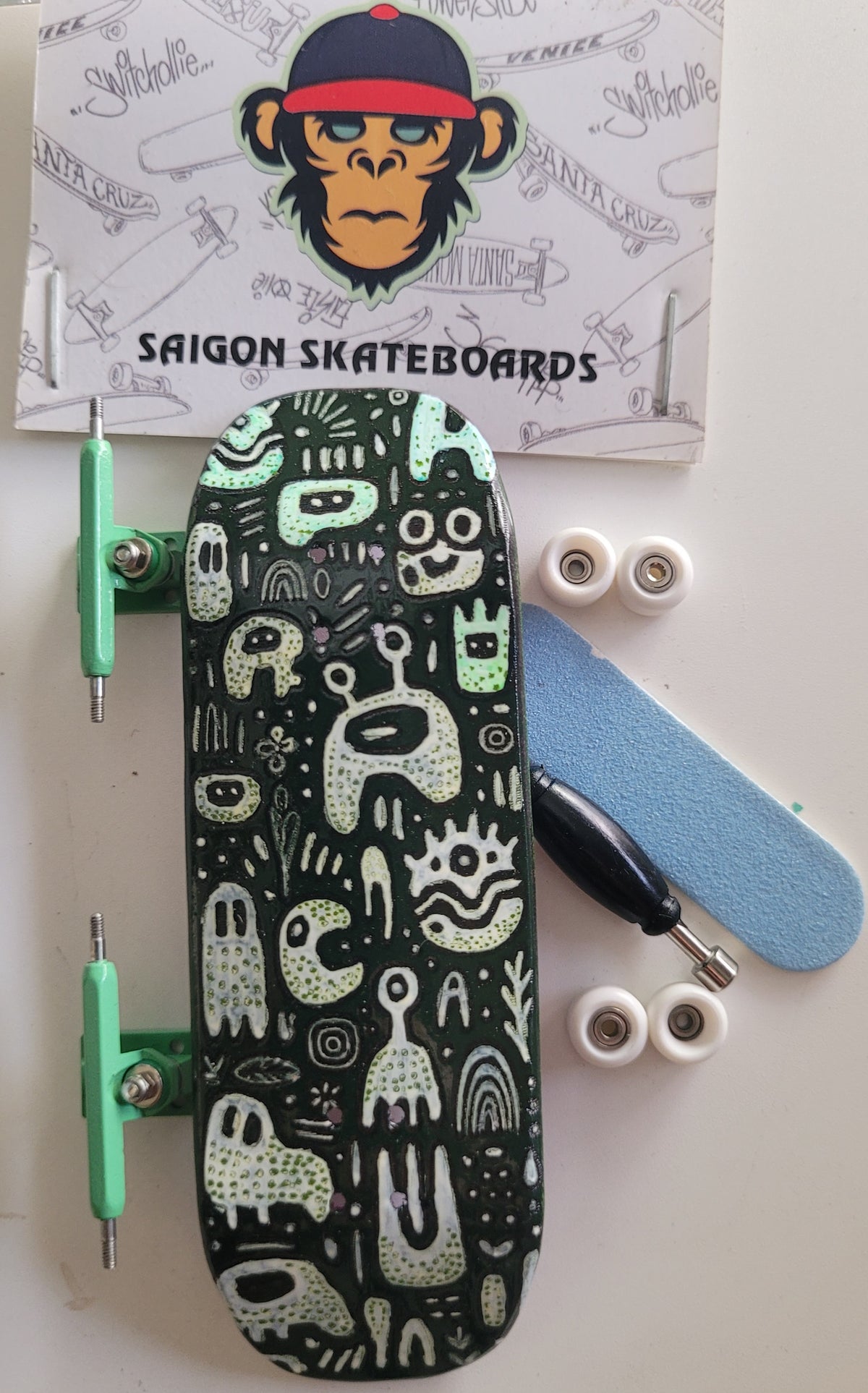 Medium fingerboard with black monster doodle deck, green wheels, and silver trucks.