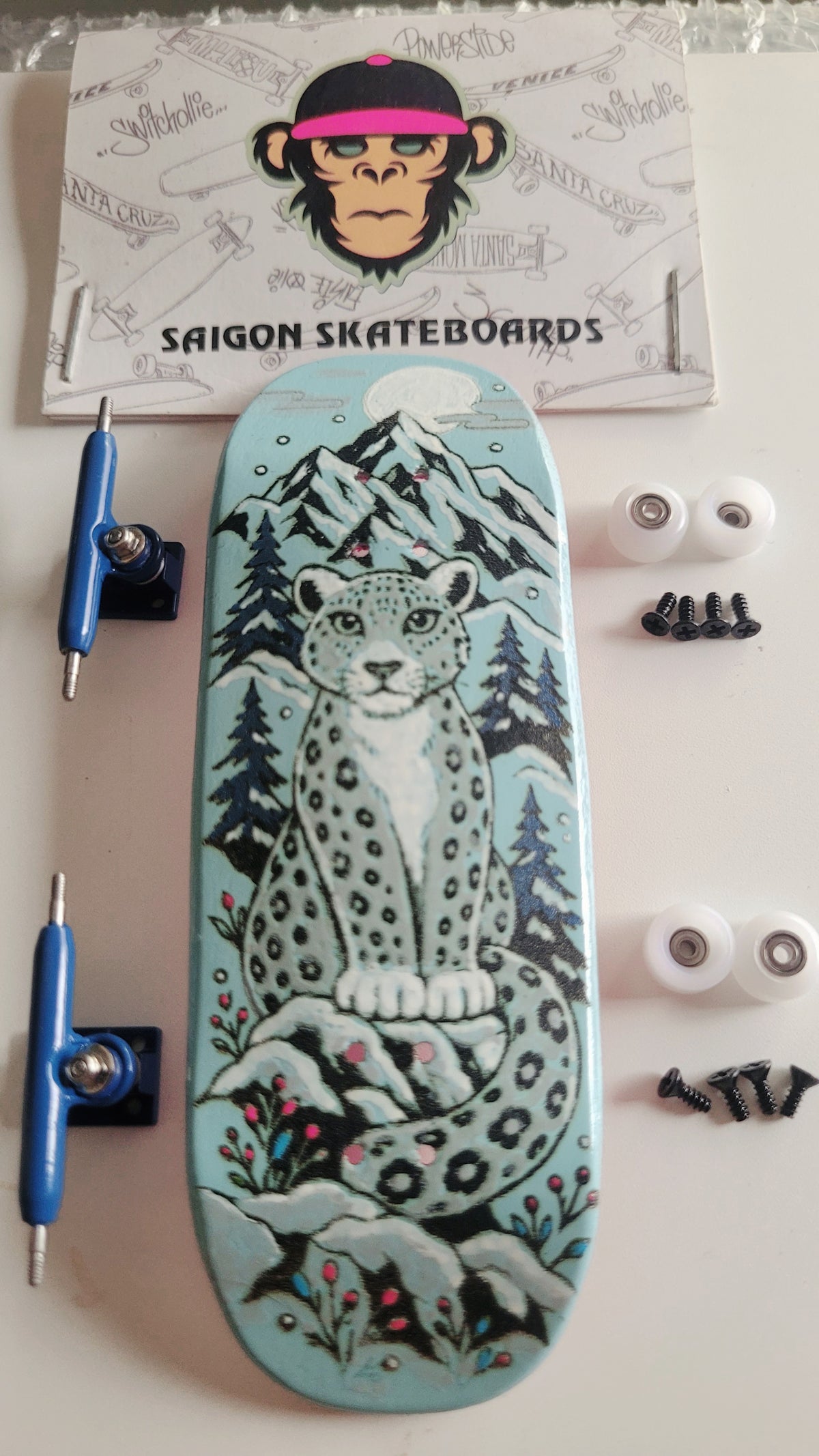 Teal finger skateboard with snow leopard deck, blue trucks and white wheels