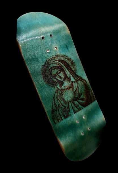 Small skateboard deck with a engraved design held in a hand.