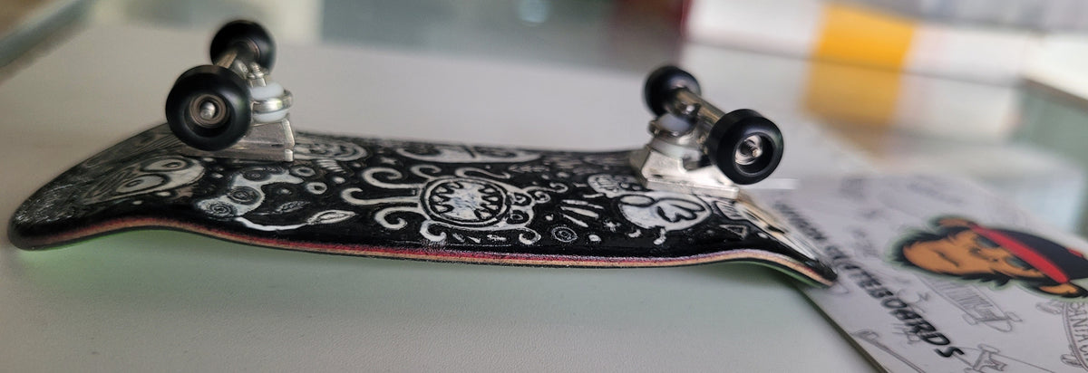 Black medium fingerboard with white monster doodle graphics and silver trucks.