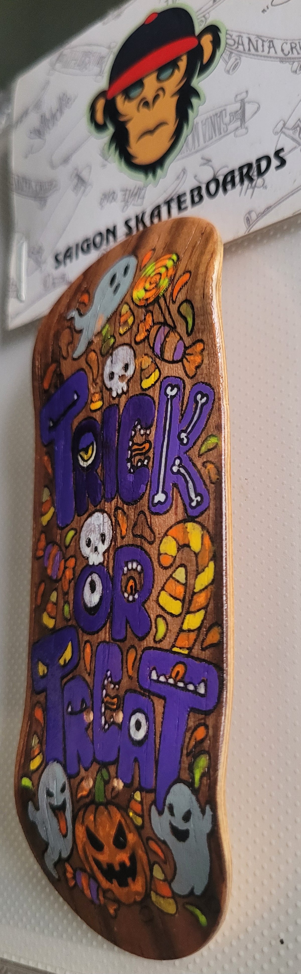 Skateboard deck angled view with Halloween icons and purple “TRICK OR TREAT” lettering