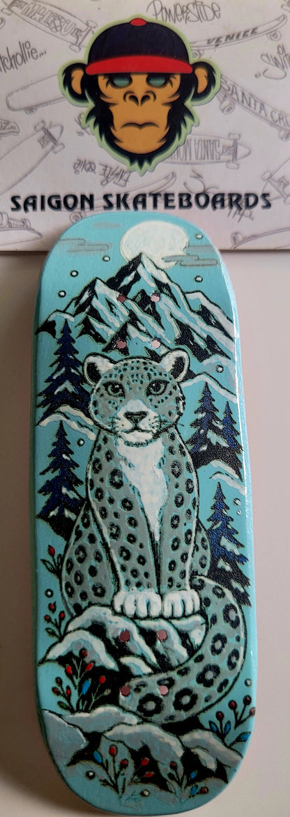 Teal finger skateboard deck with snow leopard and pine trees graphic