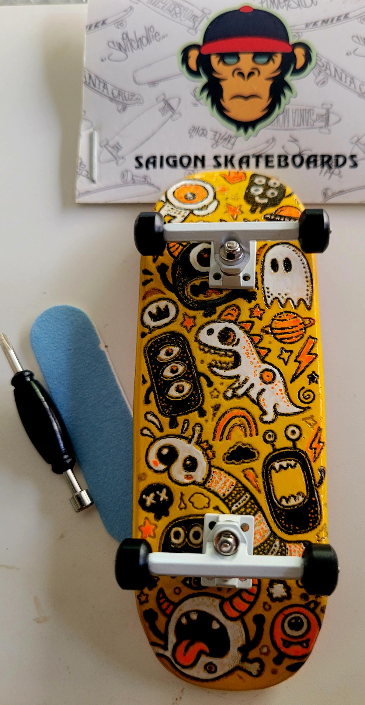 Medium fingerboard with orange monster doodle deck, black wheels, and silver trucks.