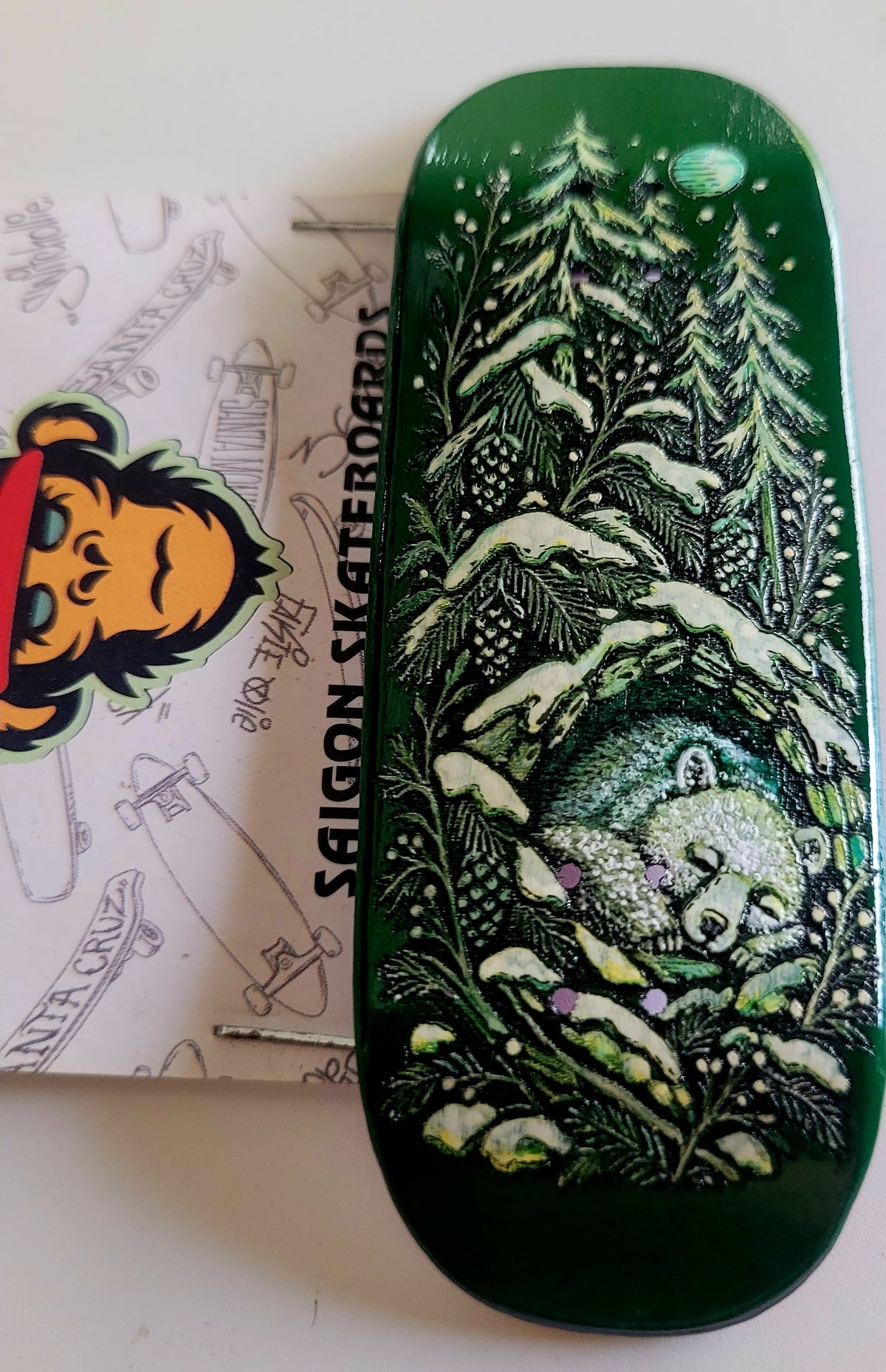 Dark green skateboard deck top view showing forest scene with moon and rolling waves