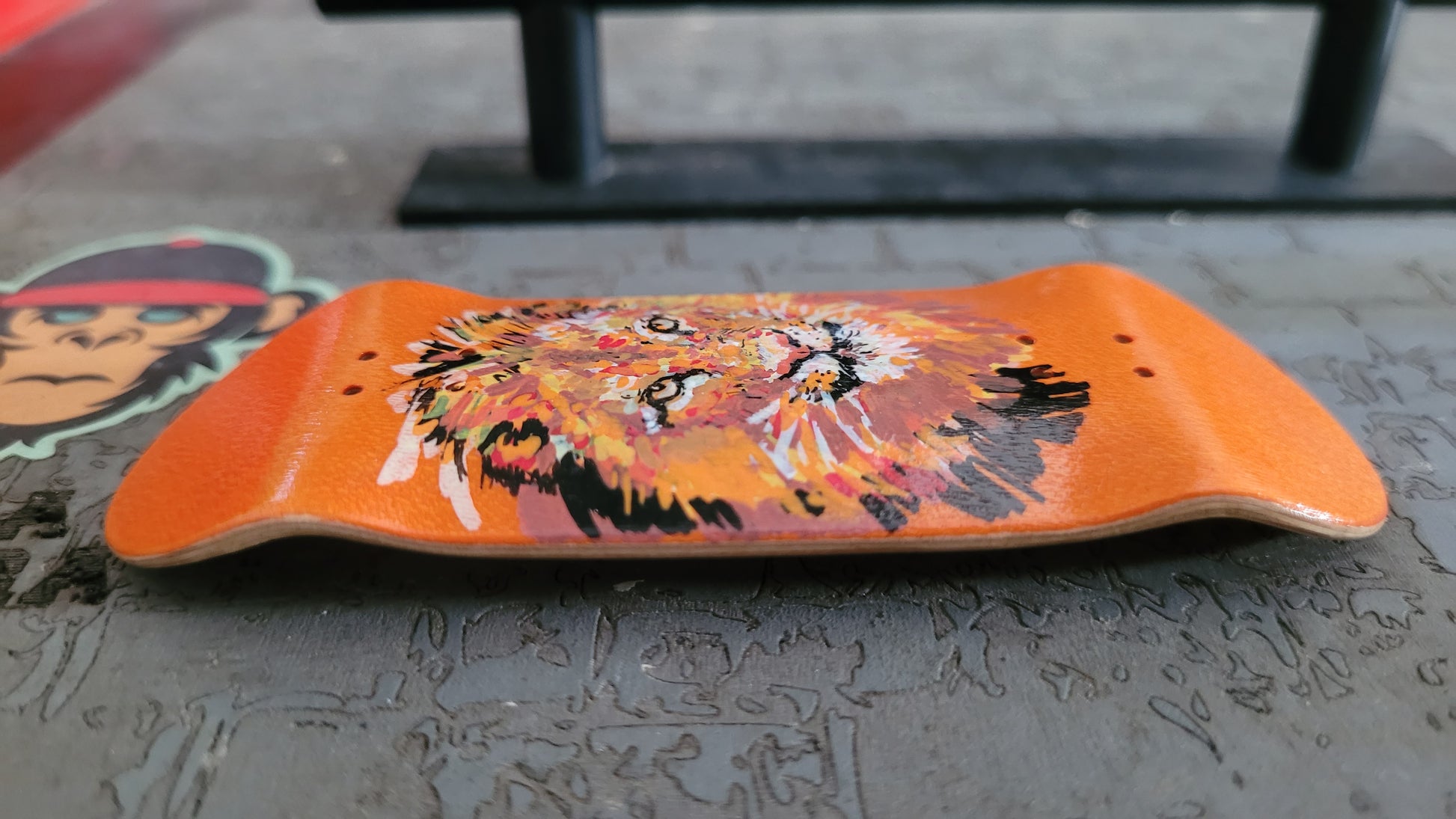 Orange fingerboard deck with lion design on a concrete surface
