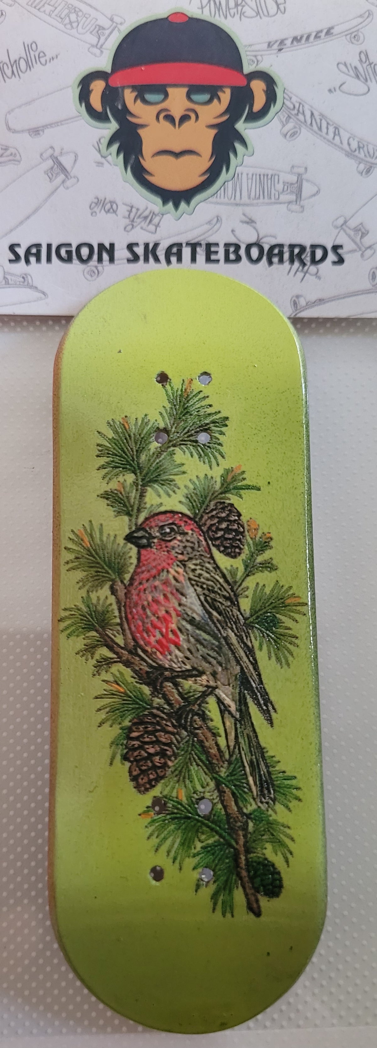 Green fingerboard deck with red bird, pine needles, and pinecone illustration