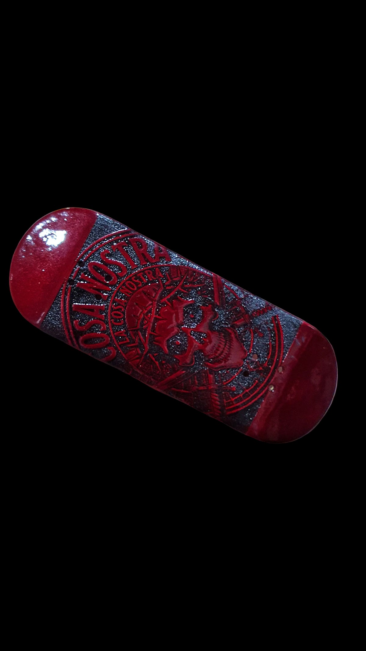 Red fingerboard deck angled view with dark central panel and skull logo