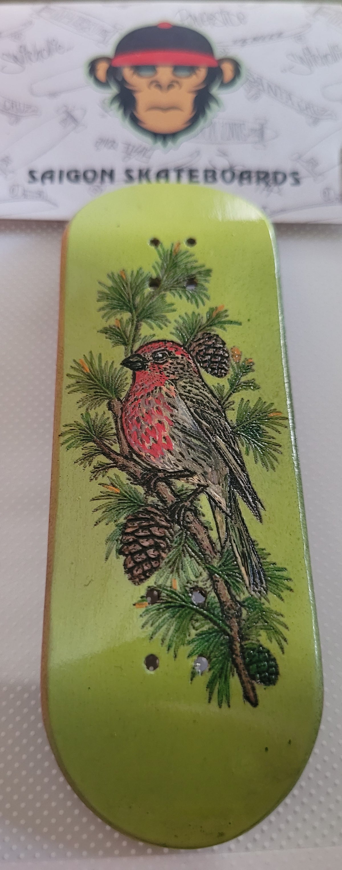 Green fingerboard with red bird and pine branch graphic on deck