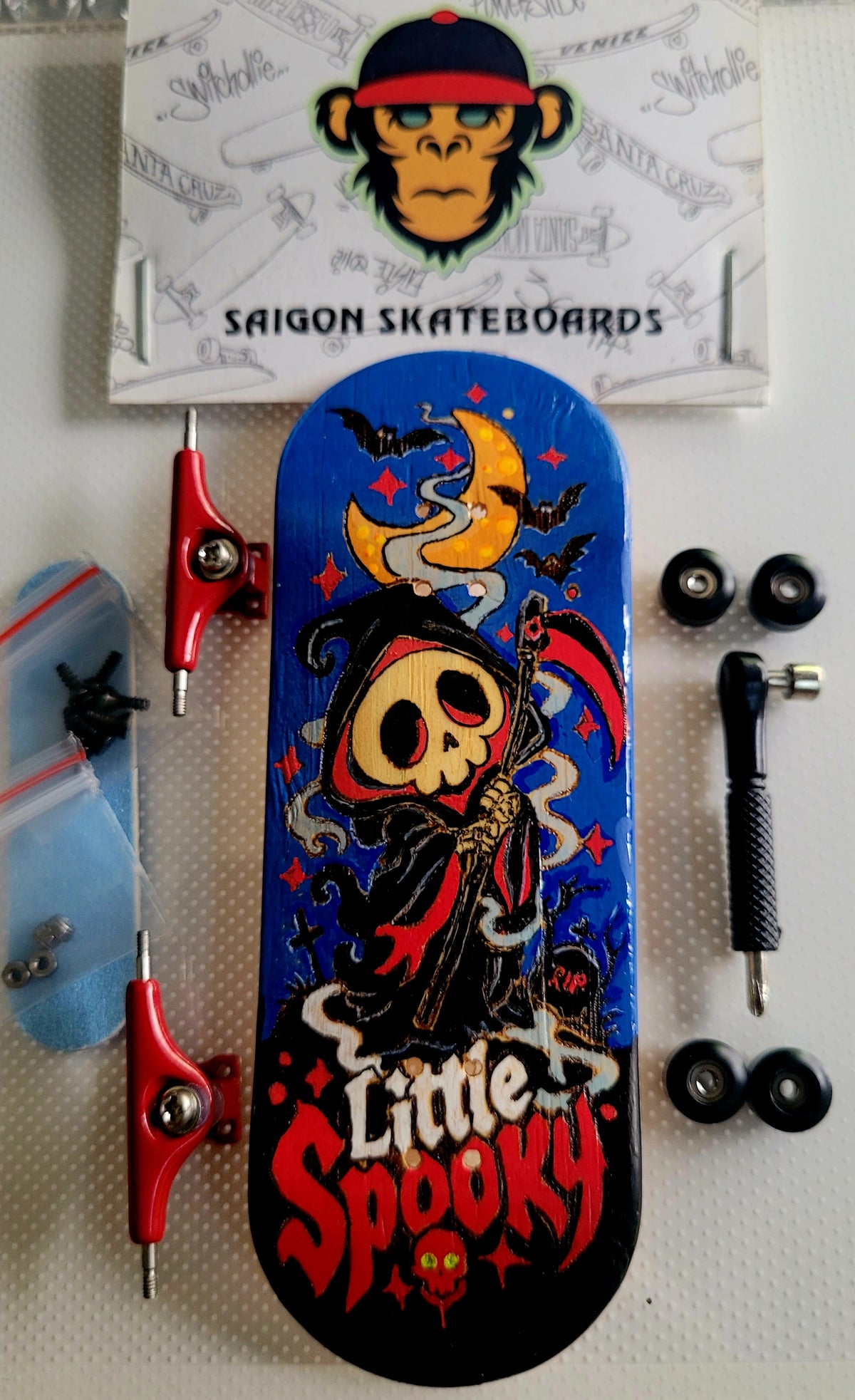 Fingerboard with blue deck, red trucks and wheels, and witch skull "Little Spooky" graphic