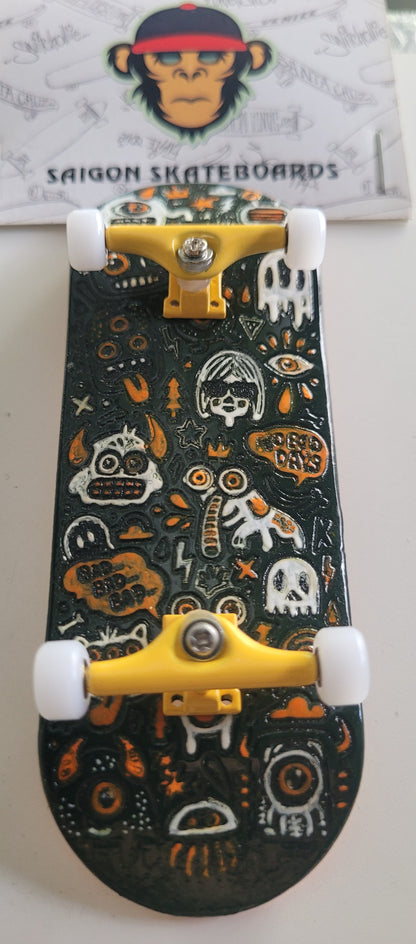Black medium fingerboard with white monster doodles, yellow trucks, and white wheels.
